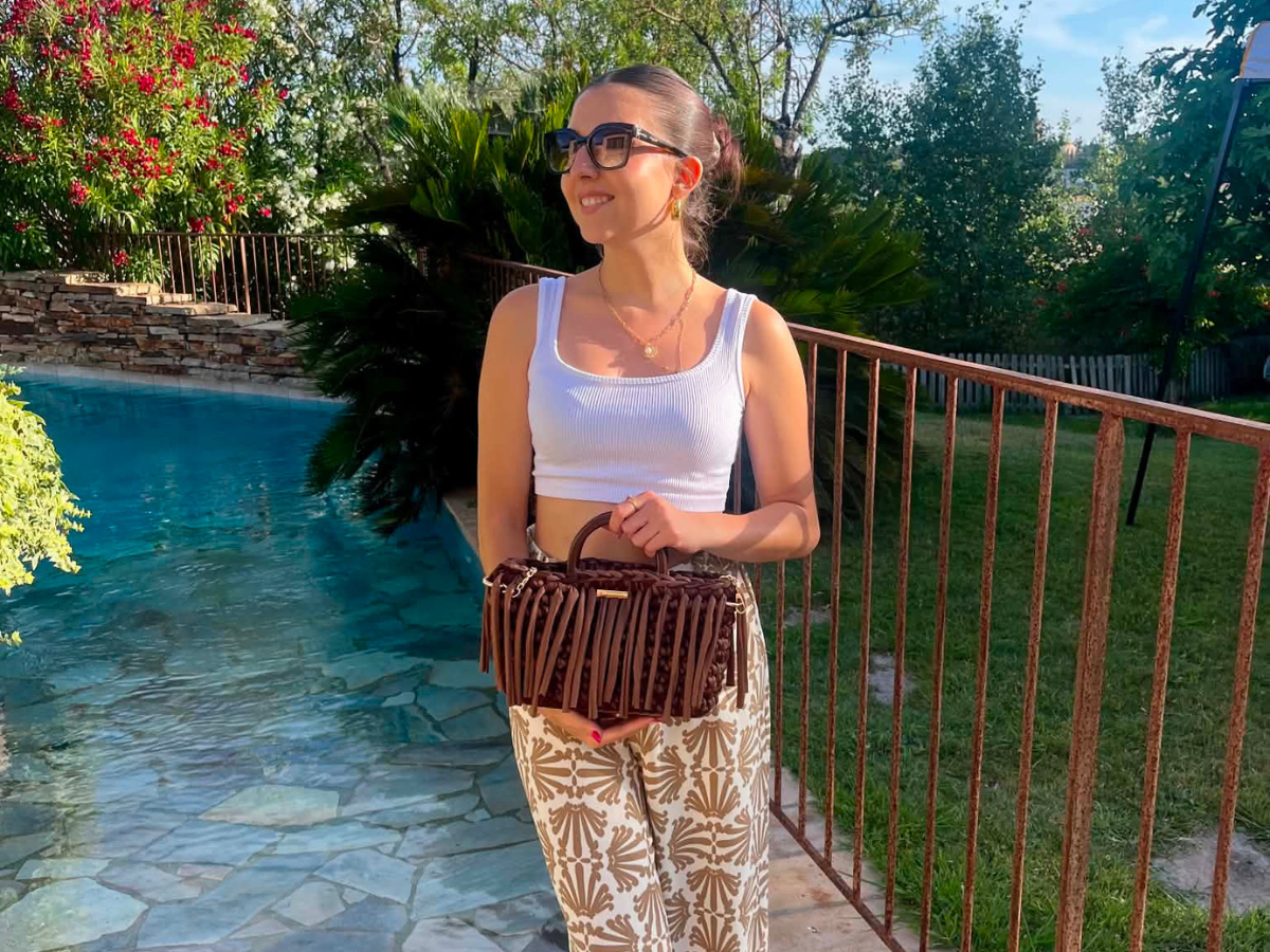 Femme tenant un sac Marie crocheté marron Laurette Créations au bord d'une piscine