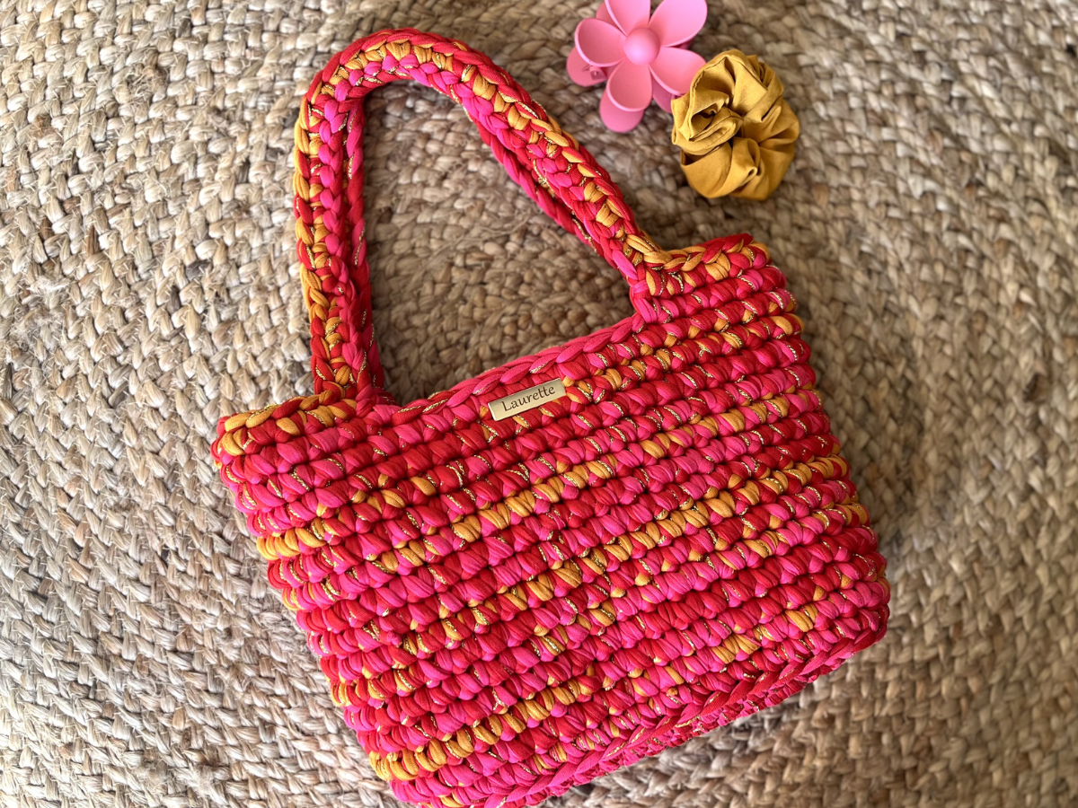Tote Bag Marcelle en crochet Laurette Créations rose corail et doré posé sur tapis en fibre naturelle